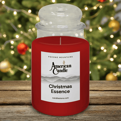 American Candle Christmas Essence Scented Jar Candle with a Christmas tree in the background on wooden table