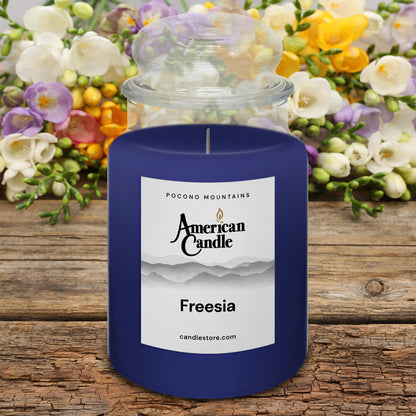 American Candle Freesia scented jar candle on a wooden table with flowers in the background