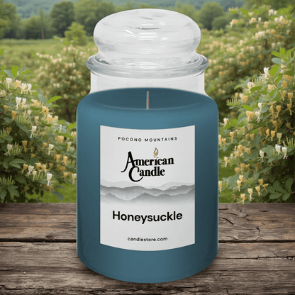 American Candle Honeysuckle Scented Jar Candle on a Wooden Table in fron of a Honeysuckle Orchard