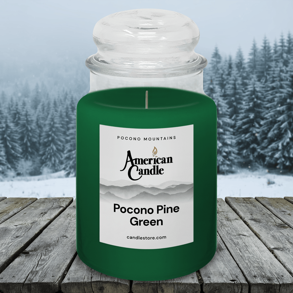American Candle Pocono Pine Green Scented Jar Candle on a Wooden Table in front of Wintery Pine Trees