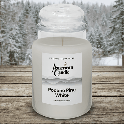American Candle Pocono Pine White scented jar candle on a wooden table with a snowy pocono pines forest trees background